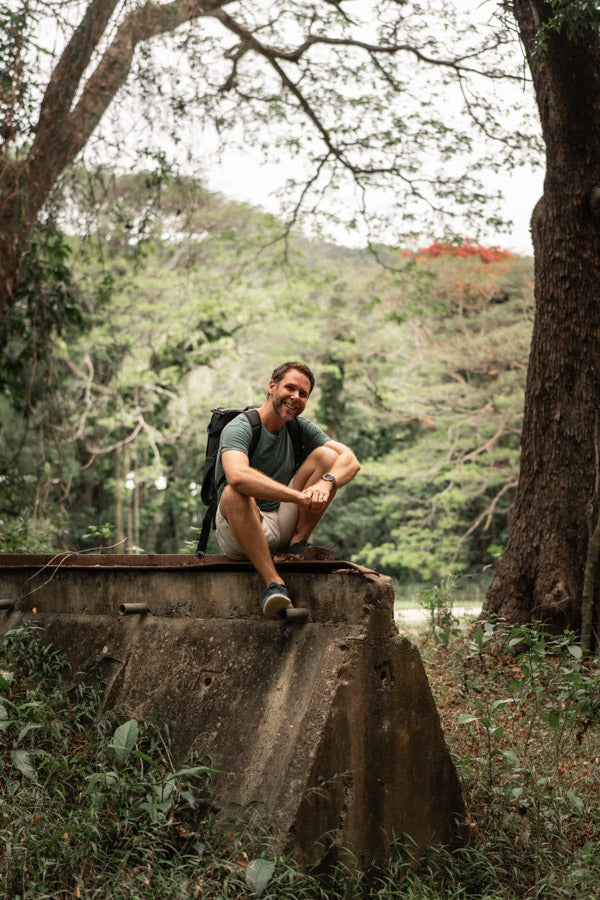 David Lloyd sitting in the rainforest, smiling with his camera gear | About Page Portrait