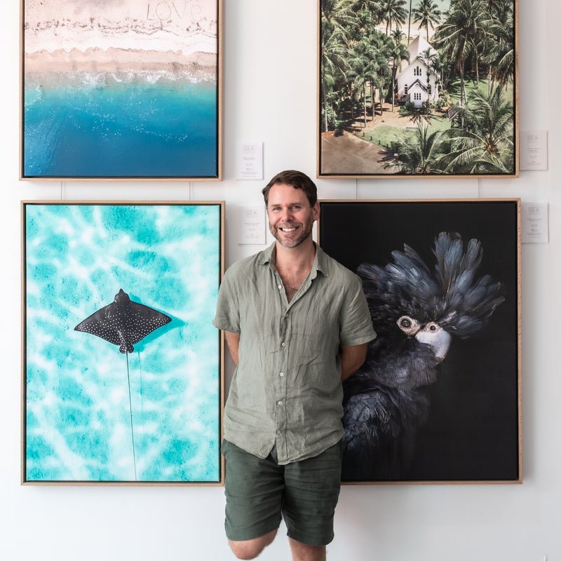 David Lloyd – portrait standing in front of gallery wall with his photographic canvas artworks displayed, warm lighting, smiling | Headshot with Artworks