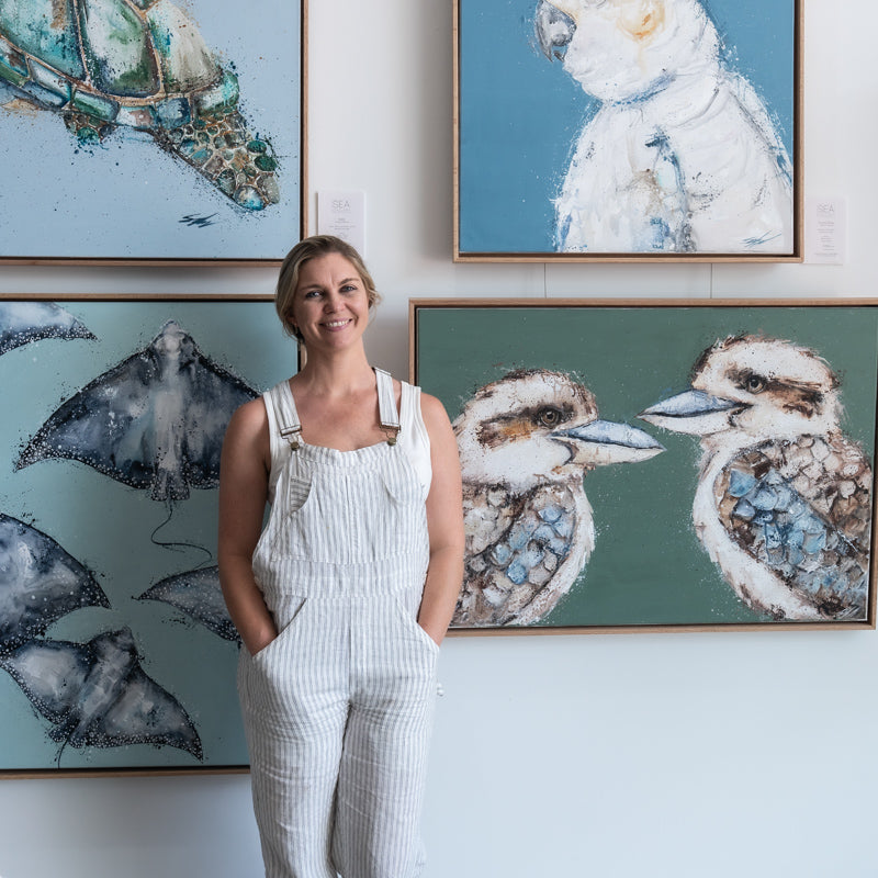 Stephanie Elizabeth – portrait standing in front of gallery wall with her canvas artworks displayed, warm lighting, smiling | Headshot with Artworks