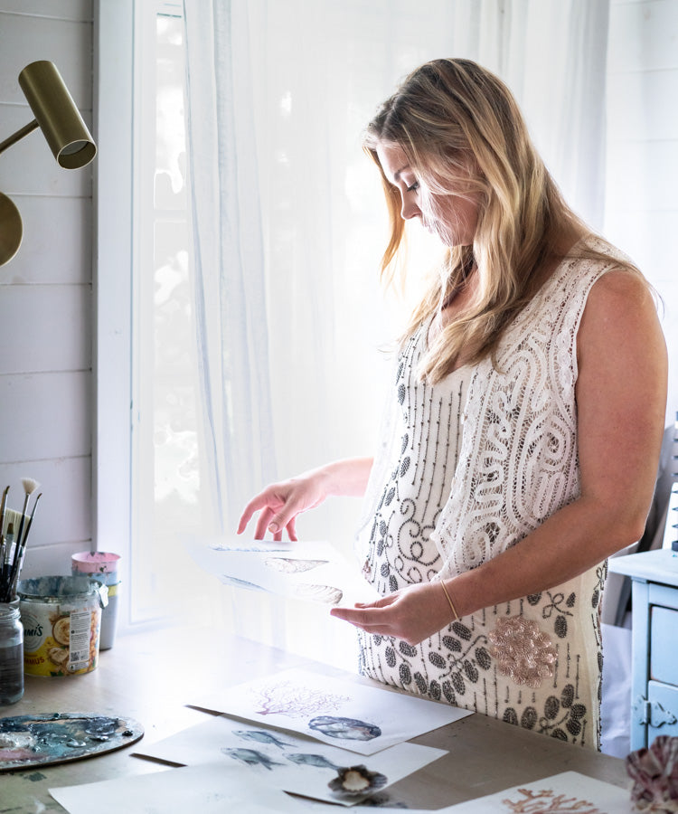 Stephanie Elizabeth looking over one of her artworks in the studio, reflecting on the creative process | About Page Section “A Sea of Change”