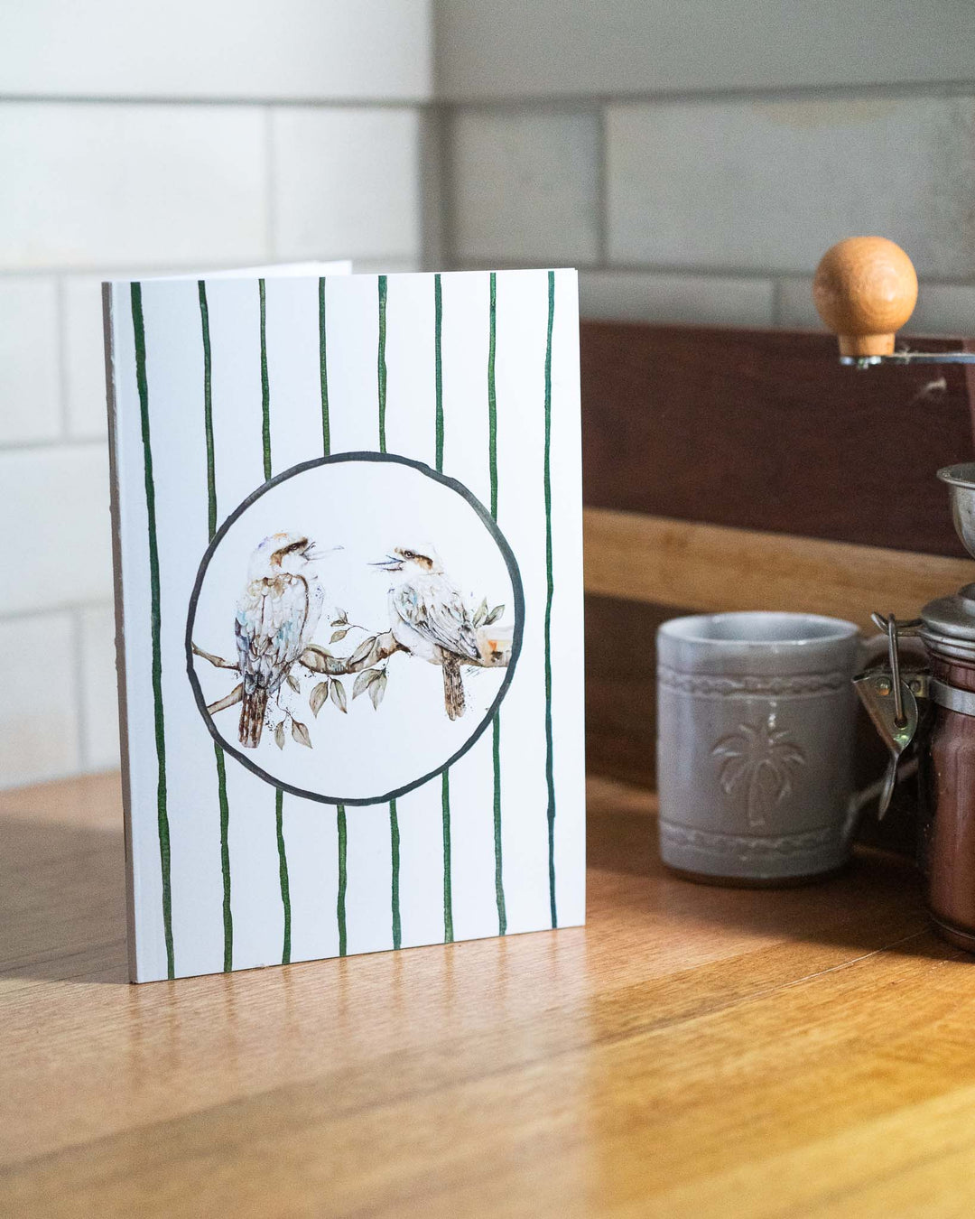 “Branching Out Together” A5 notebook with kookaburras on a wooden counter next to a mug.