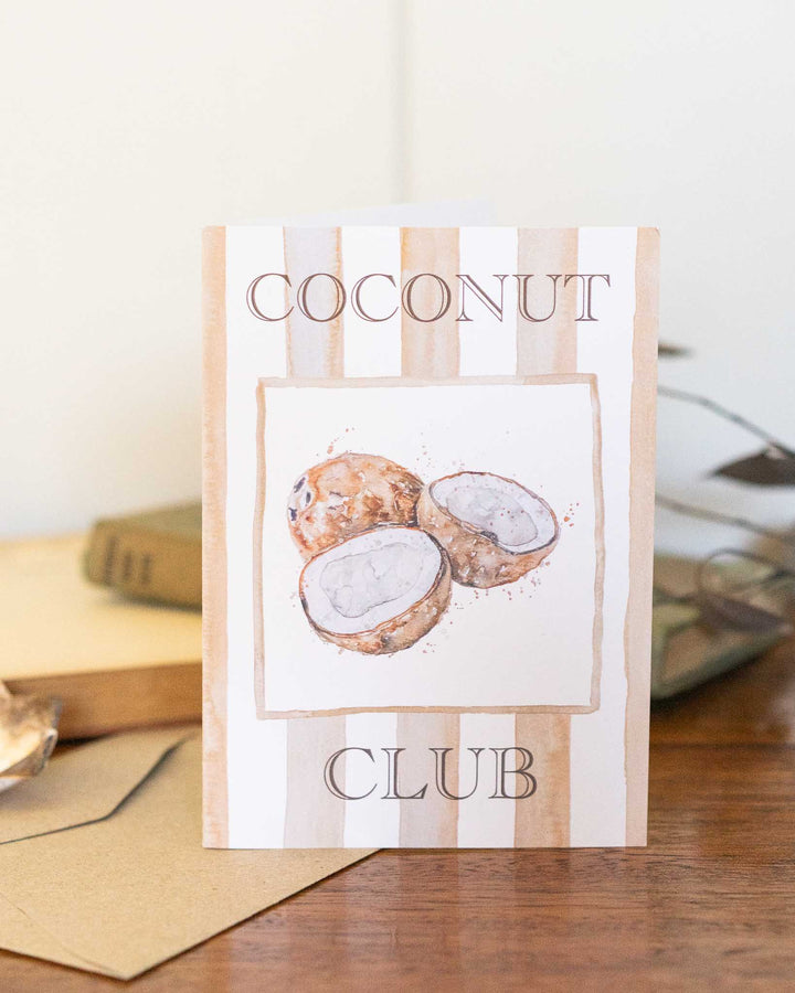 Coconut Club greeting card showing three cracked coconuts resting on a wooden surface.