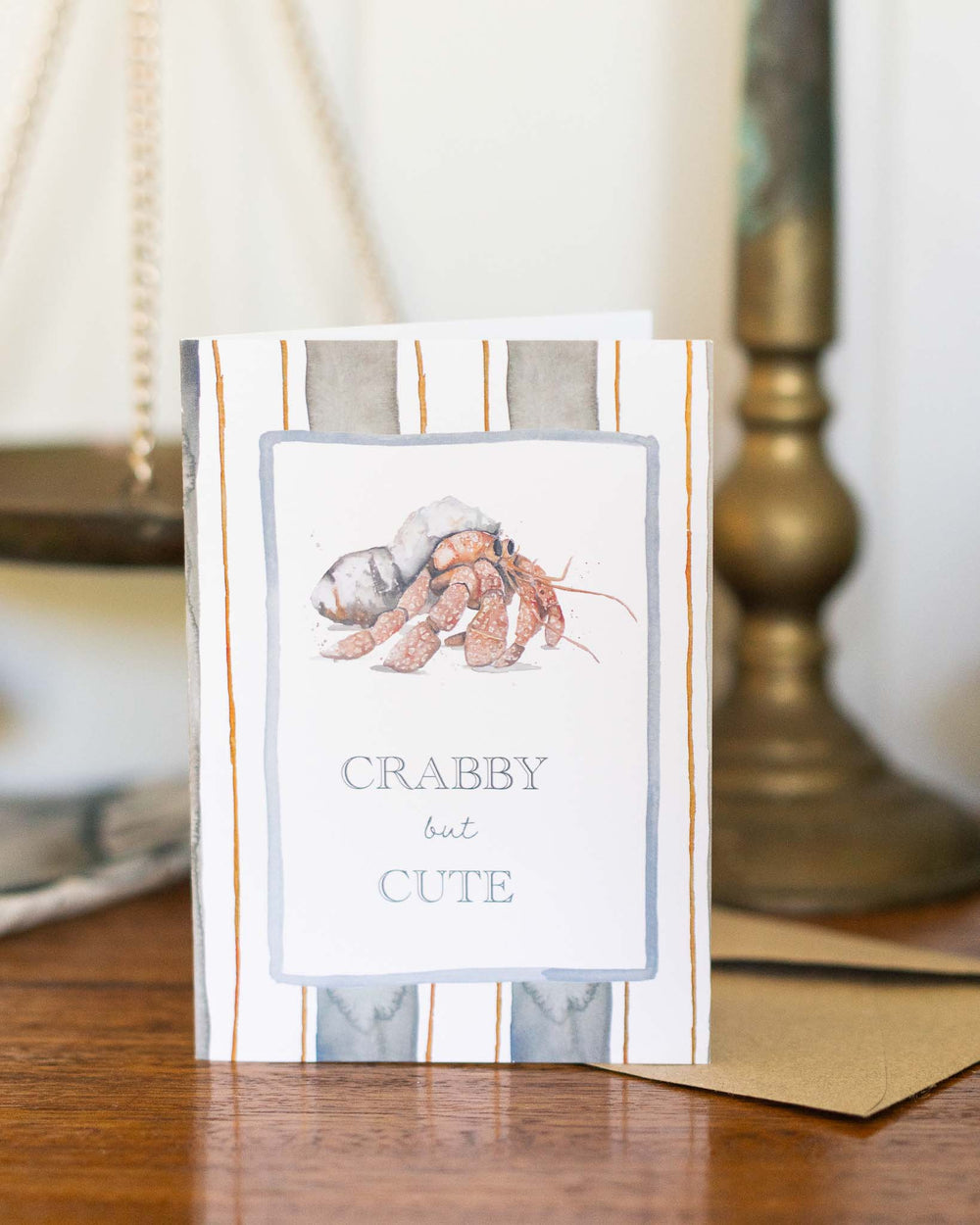 Crabby But Cute greeting card featuring a watercolor hermit crab on a wooden table.