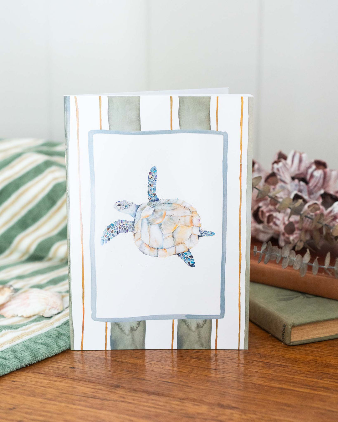 “Follow Me” A5 lined notebook placed next to flowers on a striped wooden surface.
