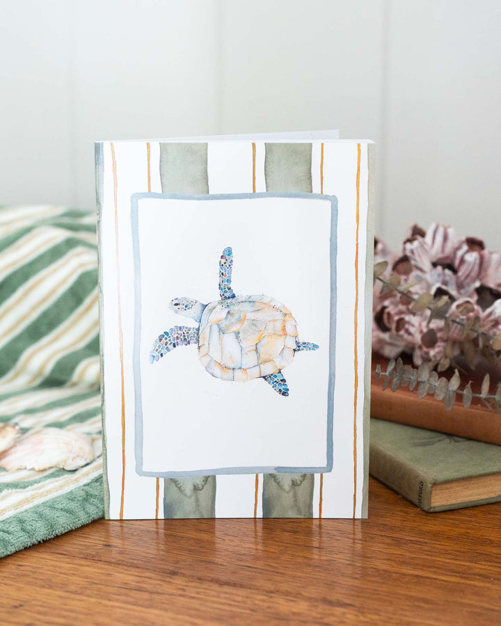 “Follow Me” A5 lined notebook placed next to flowers on a striped wooden surface.