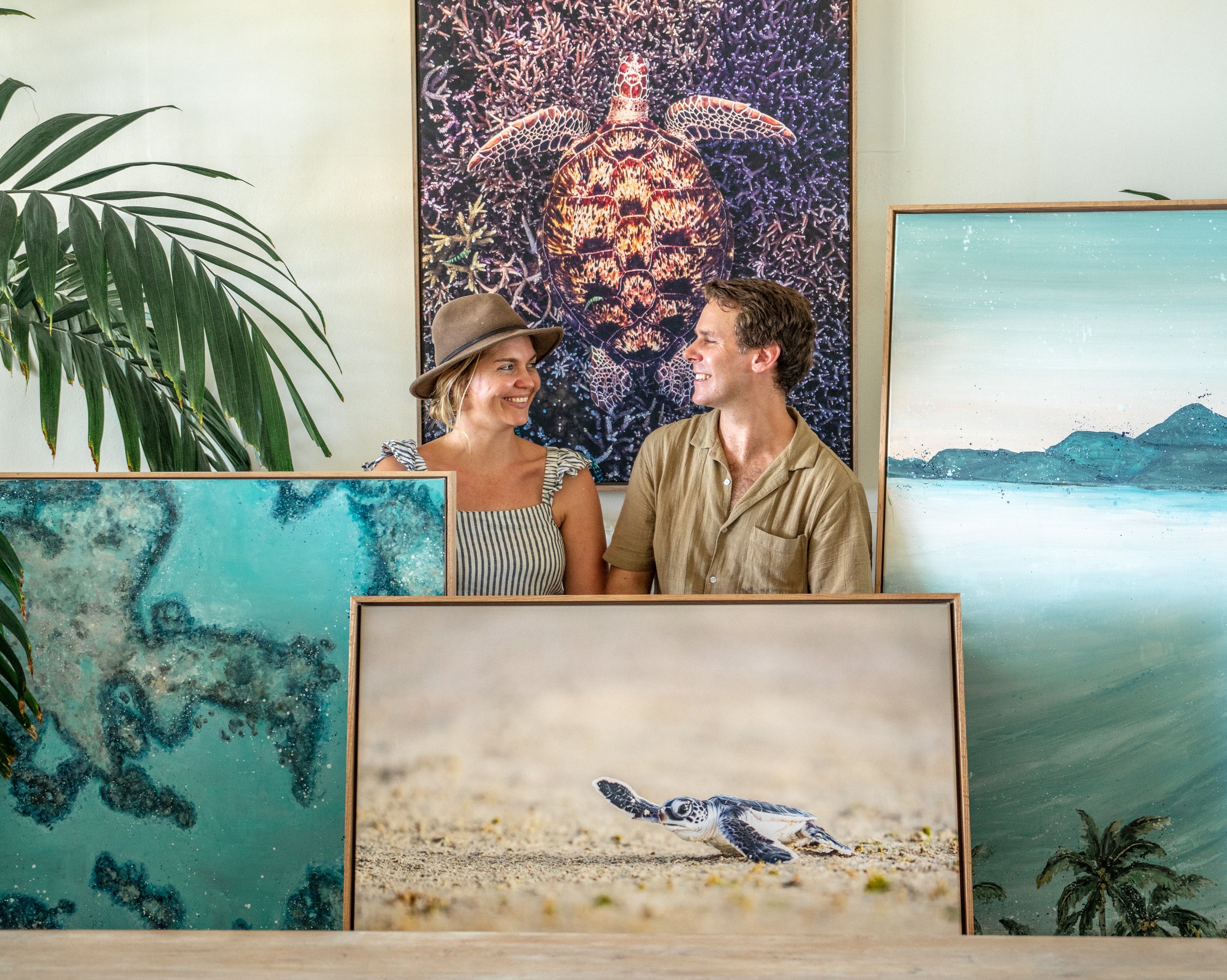 A couple smiling at each other, standing by framed ocean and sea turtle wall art.