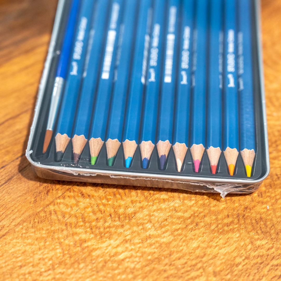 SEA Gallery Jasart 12 Watercolour Pencil Set in a metal case, pencils organized on a wooden surface.