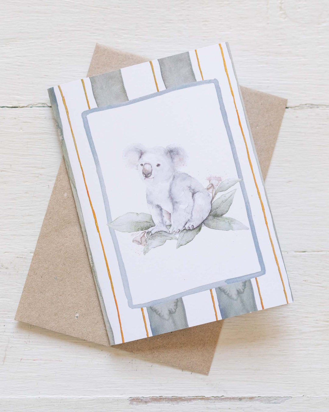 Koala Bloom greeting card with watercolor leaves, striped border, and a matching brown envelope.