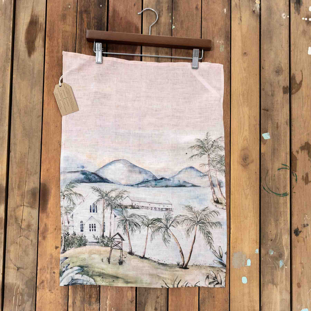 Port Douglas Linen Tea Towel with a calm landscape design, displayed on a rustic wooden hanger.