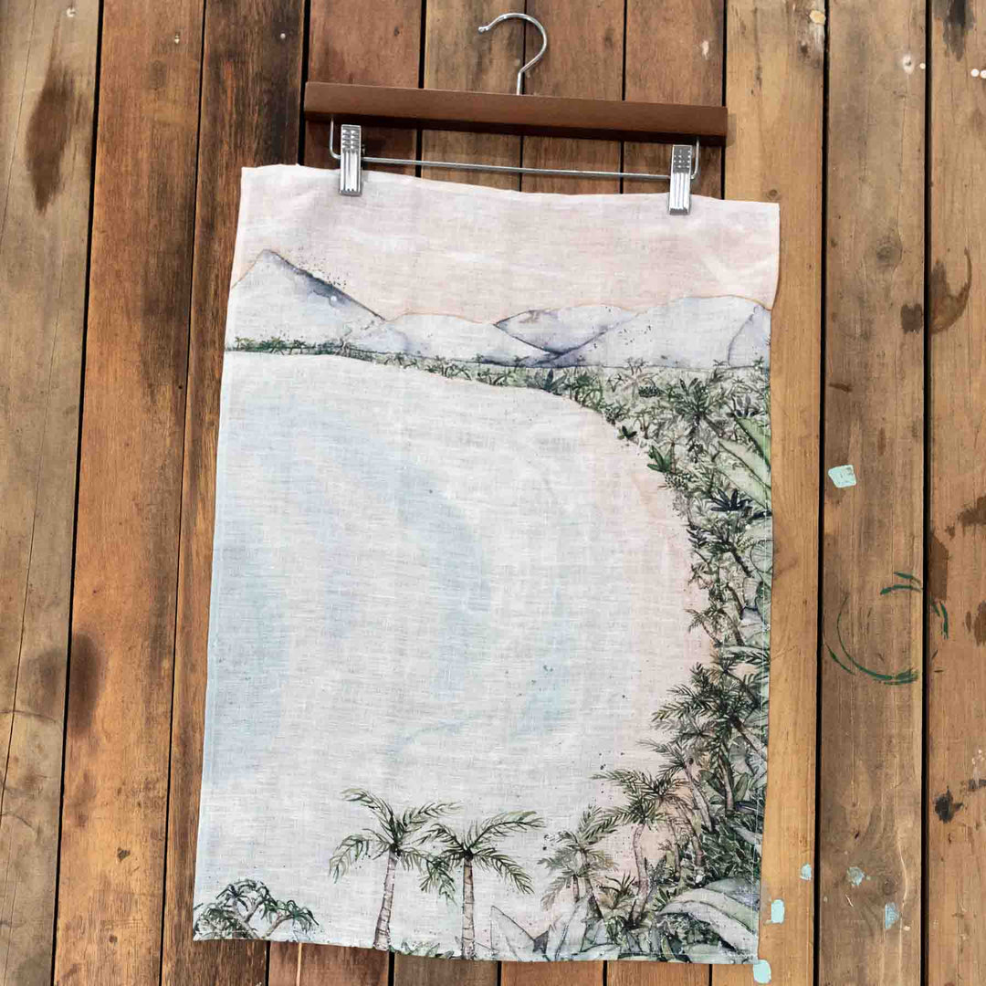 Four Mile Linen Tea Towel hangs on a wooden hanger above light natural wood flooring.