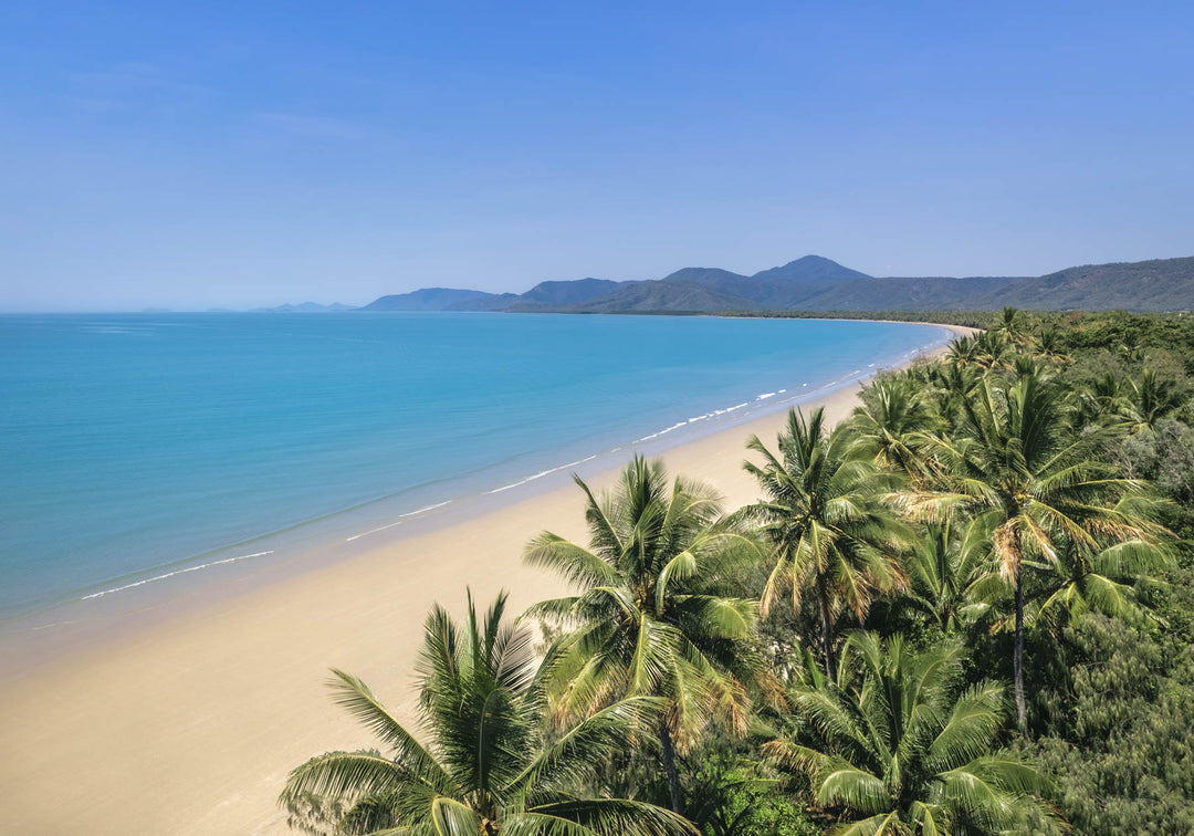 No Place I’d Rather Be – aerial view of Four Mile Beach Port Douglas with turquoise Coral Sea water, tropical green coastline and figures walking along the sand.