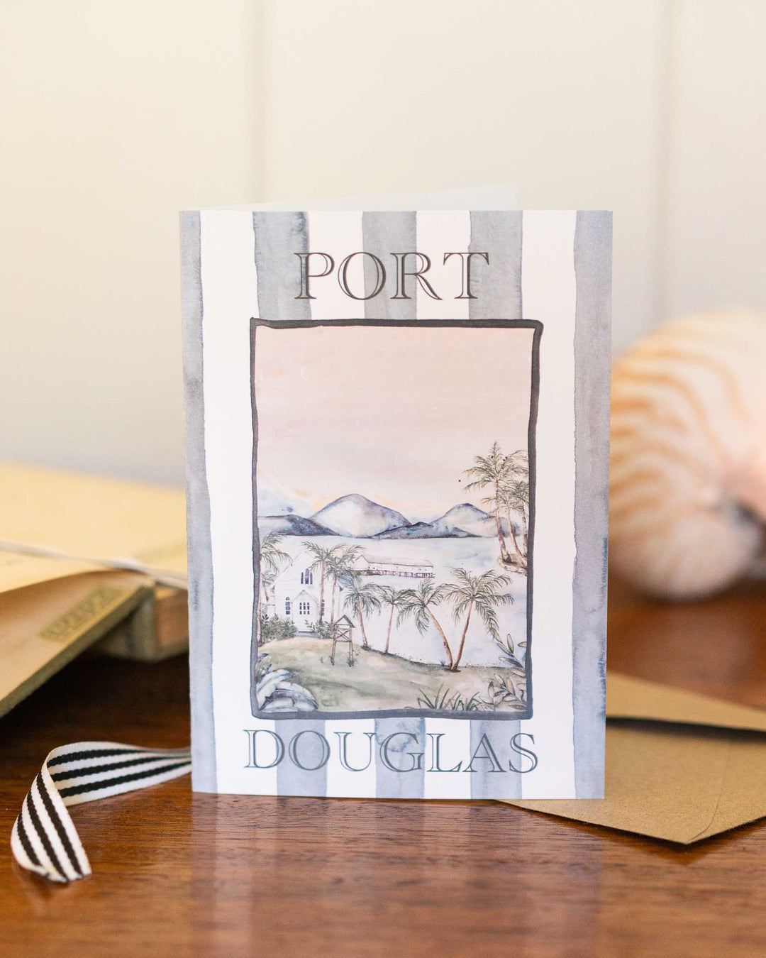 Port Douglas greeting card with envelopes and a seashell arranged on a tabletop.