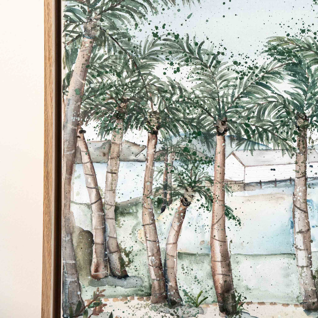 “She May Be A Hundred Different Things” watercolor of palm trees by water, framed in light wood.
