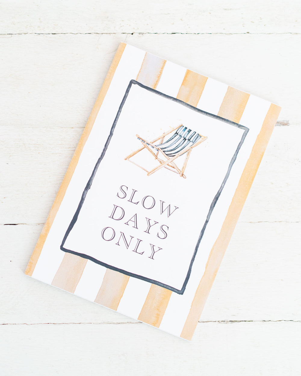 A5 lined notebook titled “SLOW DAYS ONLY” with a deck chair on a watercolor striped cover.