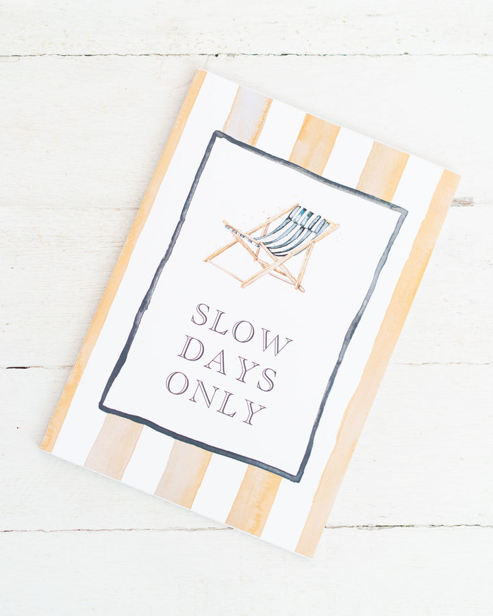 A5 lined notebook titled “SLOW DAYS ONLY” with a deck chair on a watercolor striped cover.