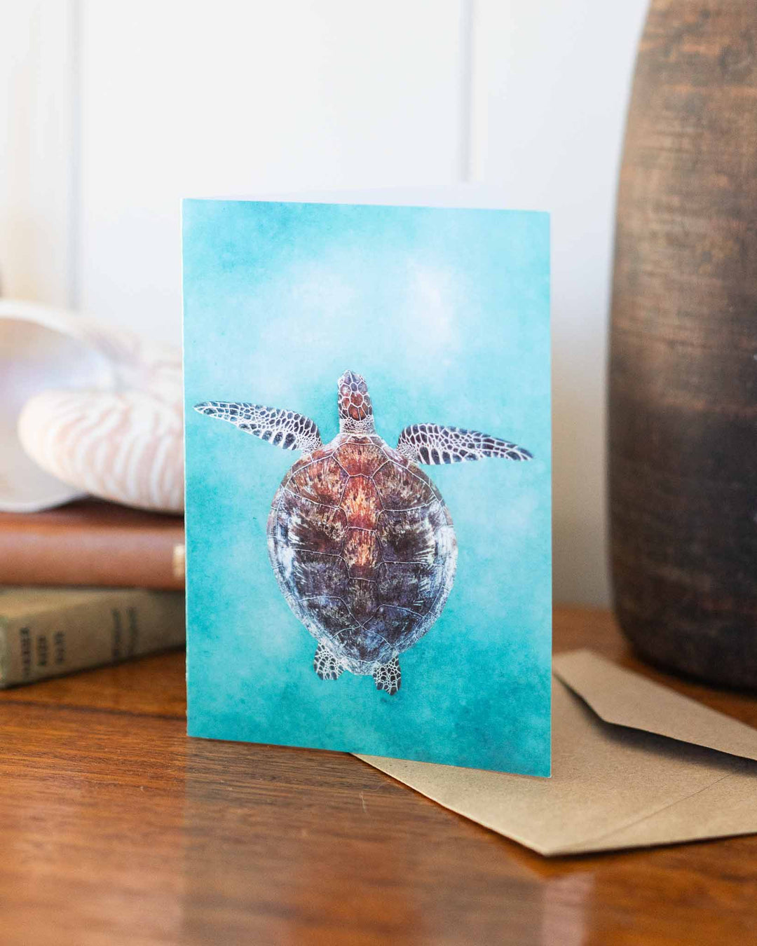 Technicolour Beat card showing a sea turtle, displayed on a wooden table with books and a shell nearby.