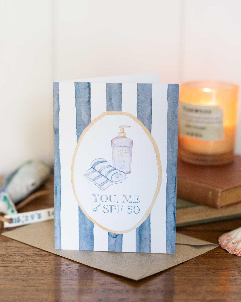 “You, Me and SPF 50” greeting card with sunscreen and towels on a colorful striped watercolor background.