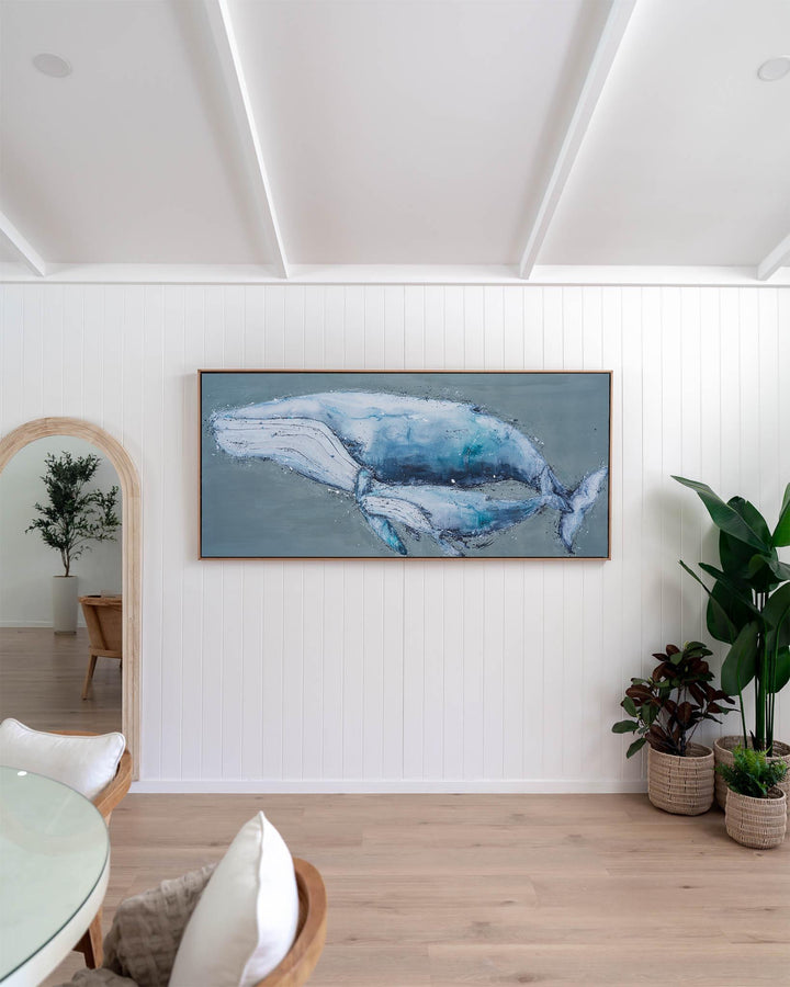 Large framed A Life Growing Together | Humpback Whales print displayed on a white paneled wall above potted plants.