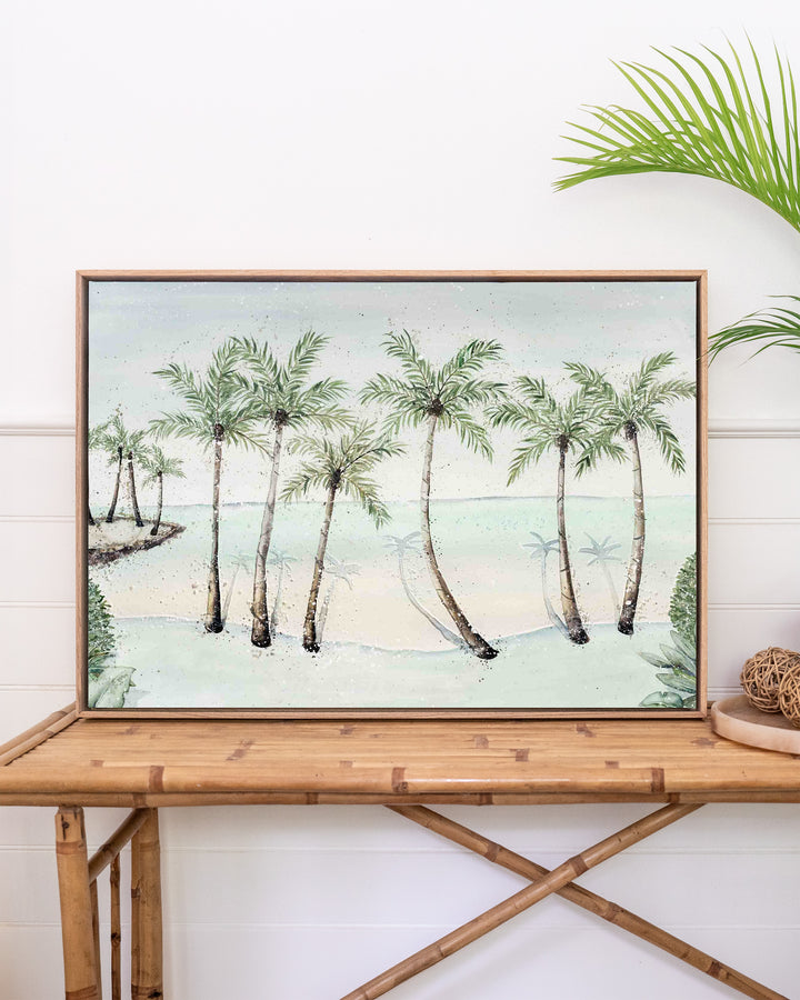 A Little Cove Love Story Port Douglas landscape fine art print by Stephanie Elizabeth, framed canvas in an oak frame above a rattan table
