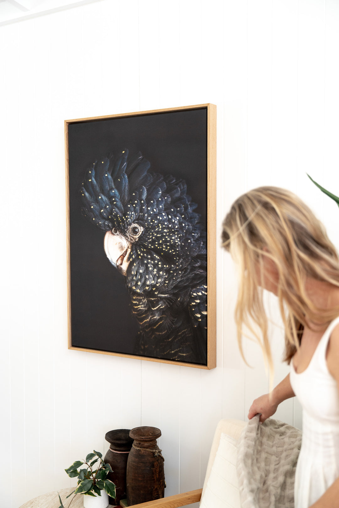 A woman adjusts a blanket beside “A Little Less Conversation” above two vases on a shelf.