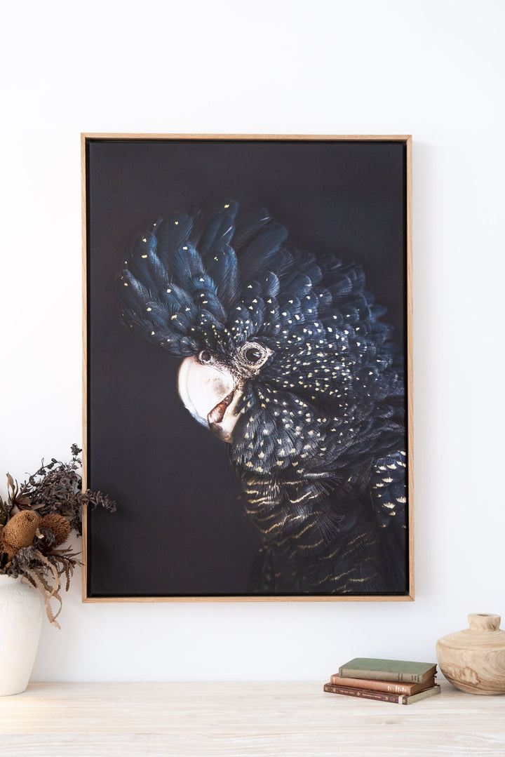 “A Little Less Conversation | Black Cockatoo” hangs above a shelf with stacked books and a single vase.