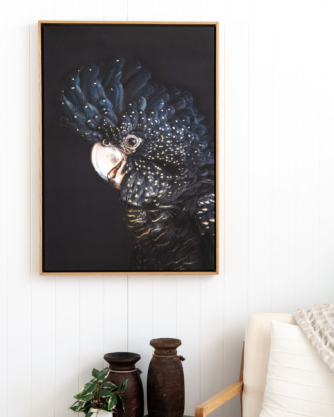 A Little Less Conversation“ Black Cockatoo artwork above plants, vases, and a white armchair.