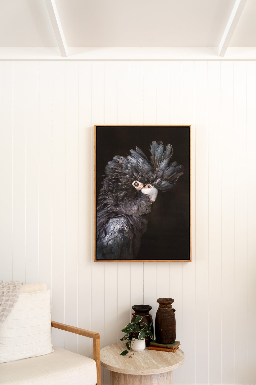 “A Little More Action” Black Cockatoo print by David Lloyd hangs above an armchair and small table.