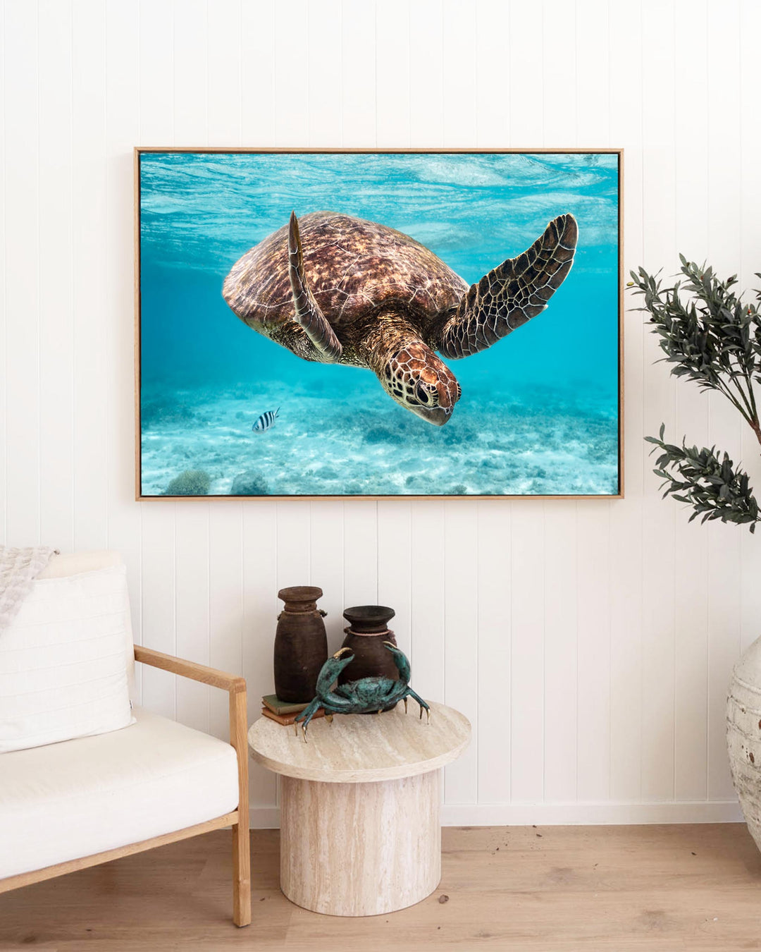 Framed A Moment Below Green Sea Turtle print hanging on a white wall above a small round table.