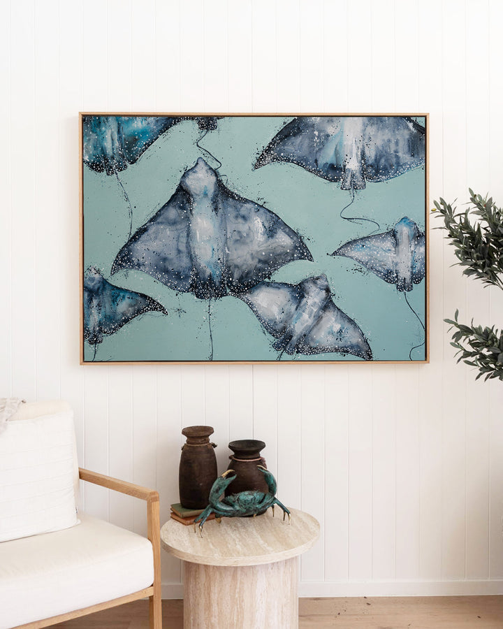 A Sea of Spots eagle rays fine art print by Stephanie Elizabeth, framed canvas in an oak frame in a living room