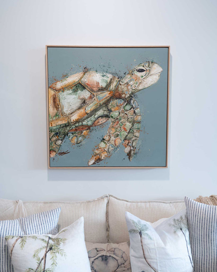A Time to Rest,“ framed sea turtle art by Stephanie Elizabeth, displayed above a beige couch in a serene setting.