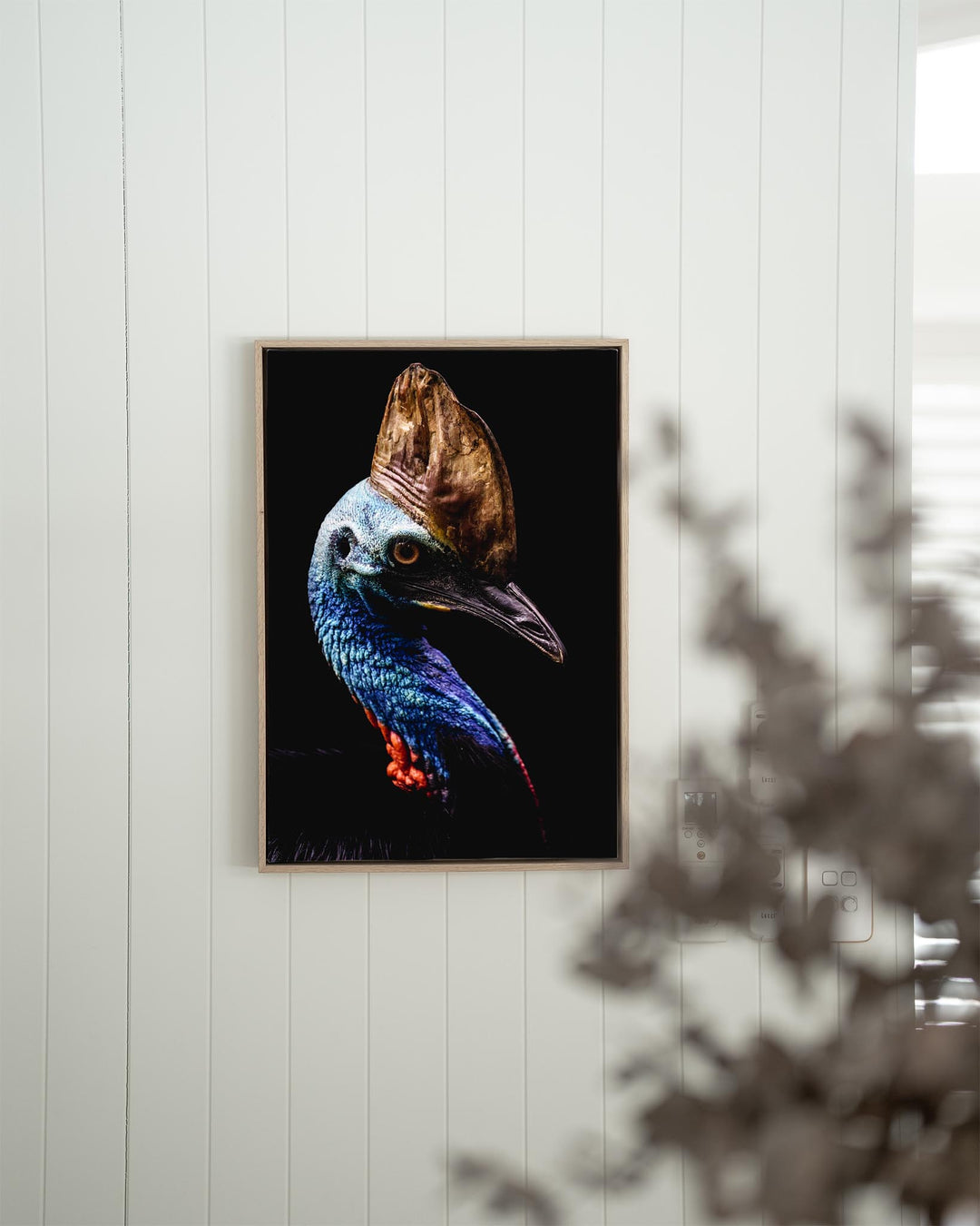 Airlie | Southern Cassowary artwork on a white wall, partially hidden by lush tropical leaves in the foreground.
