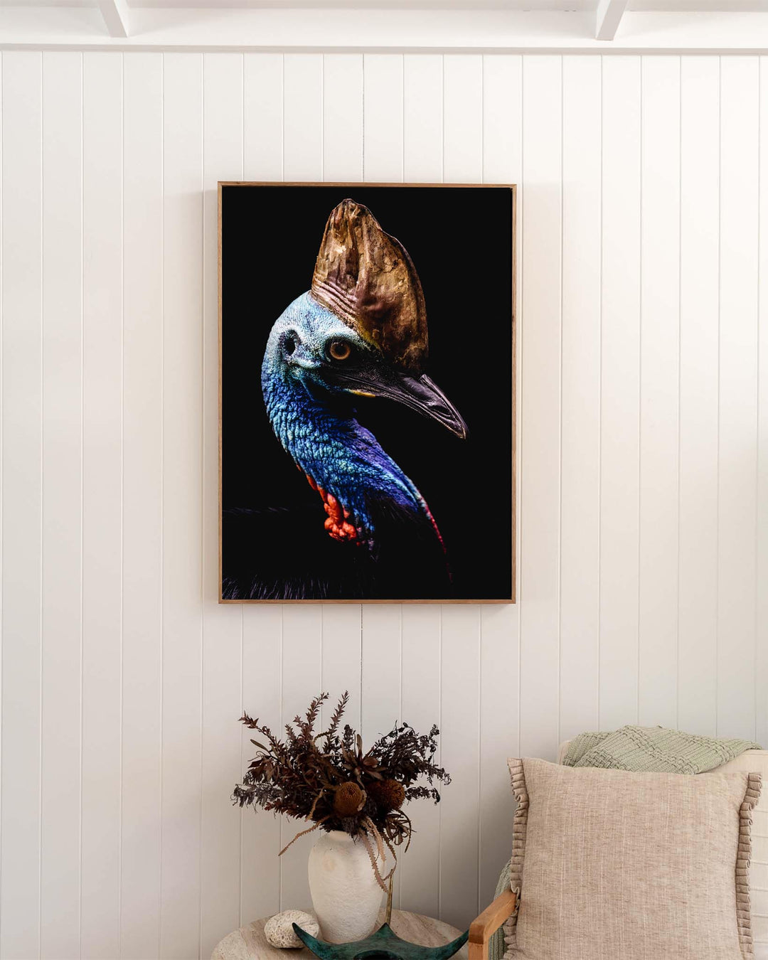 Airlie | Southern Cassowary artwork hangs above dried flowers and a beige cushion, adding a distinctive touch.