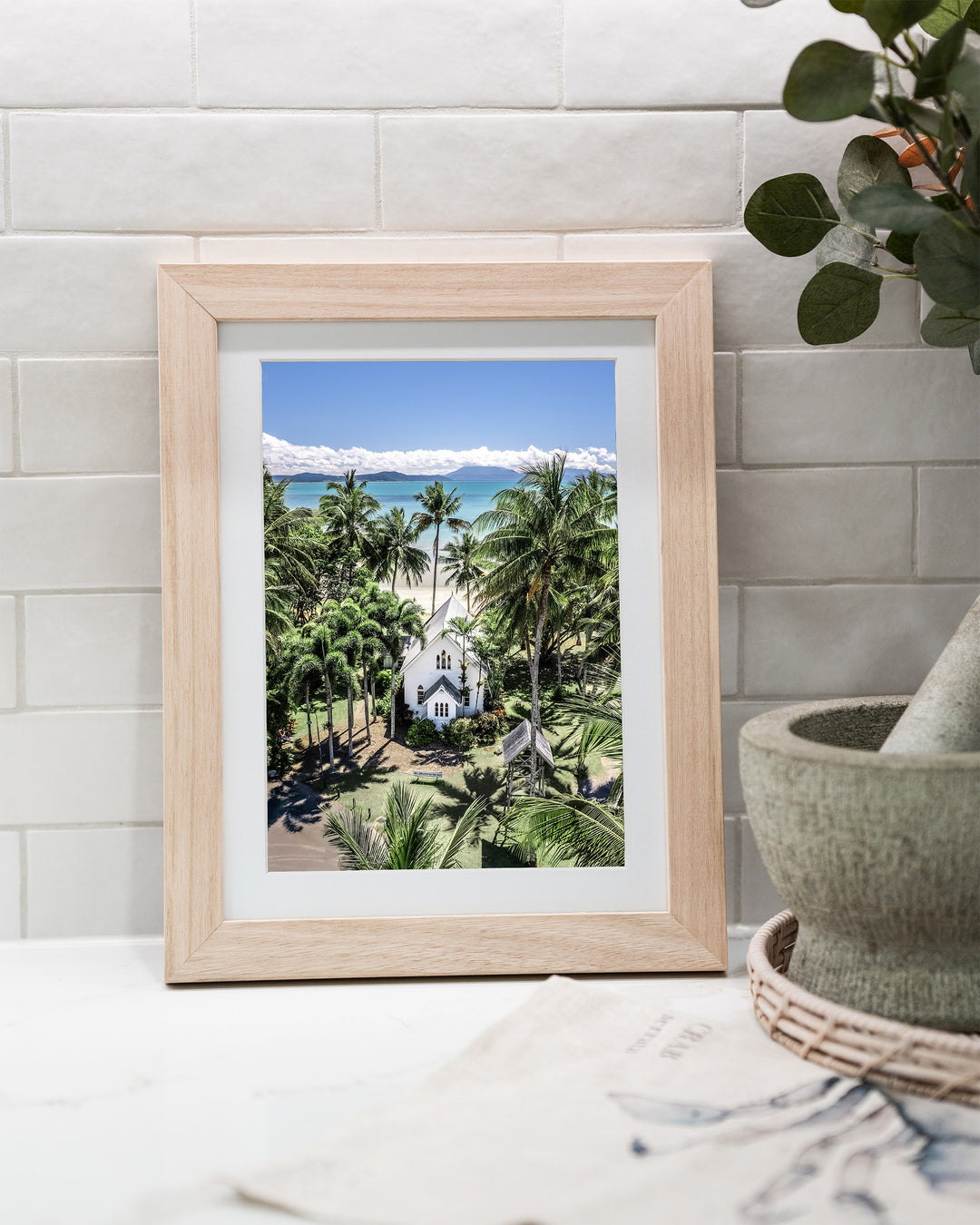 Always Forever – St Mary’s, Port Douglas, Aerial Photography by David Lloyd, framed paper print in oak frame, styled in a kitchen bench setting