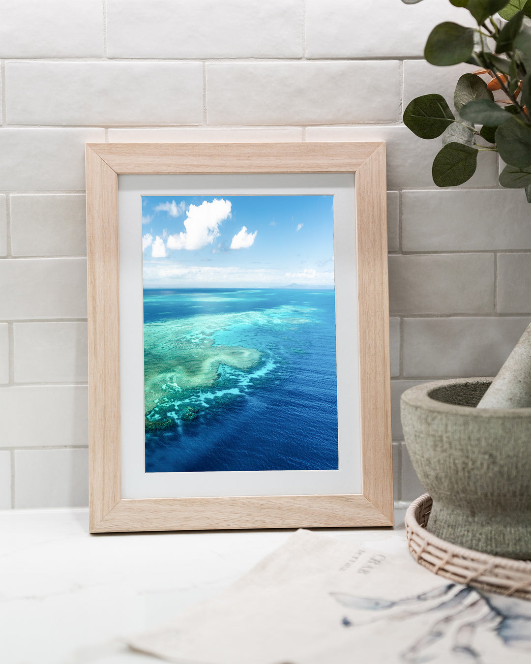 Always Take The Weather With You – Rudder Reef, Aerial Photography by David Lloyd, framed paper print in oak frame, styled in a kitchen bench setting