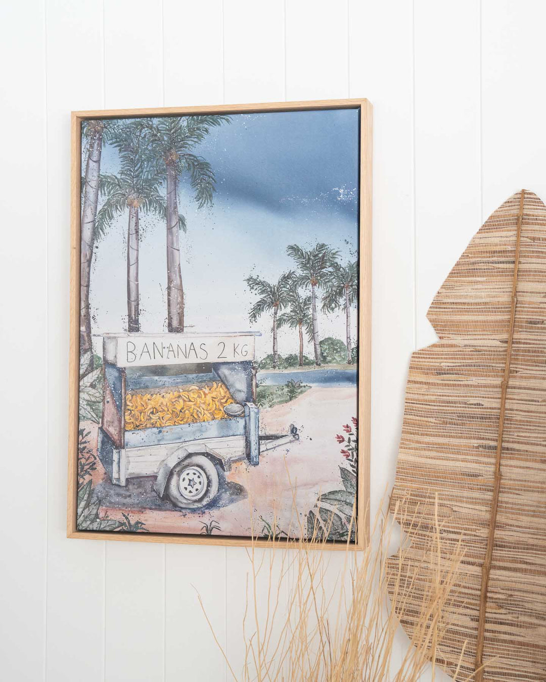 Banana Shack fine art print shows a tropical scene with lush palm trees and a banana cart under sunny skies.