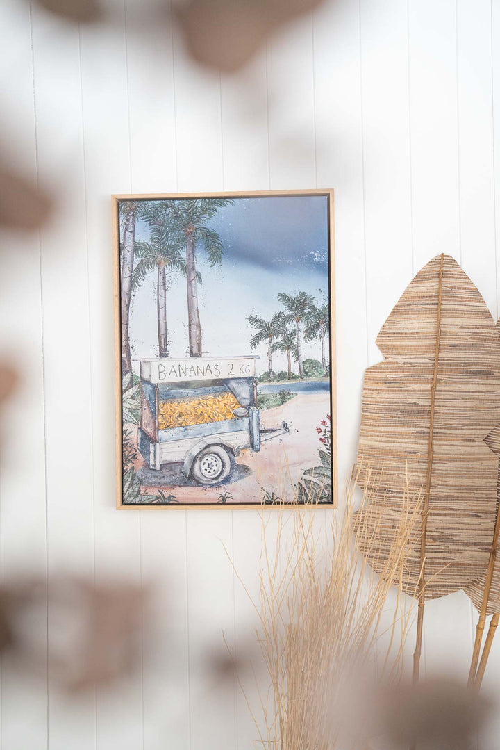 Banana Shack fine art print featuring tropical still life, displayed on a white wall with green botanical accents.