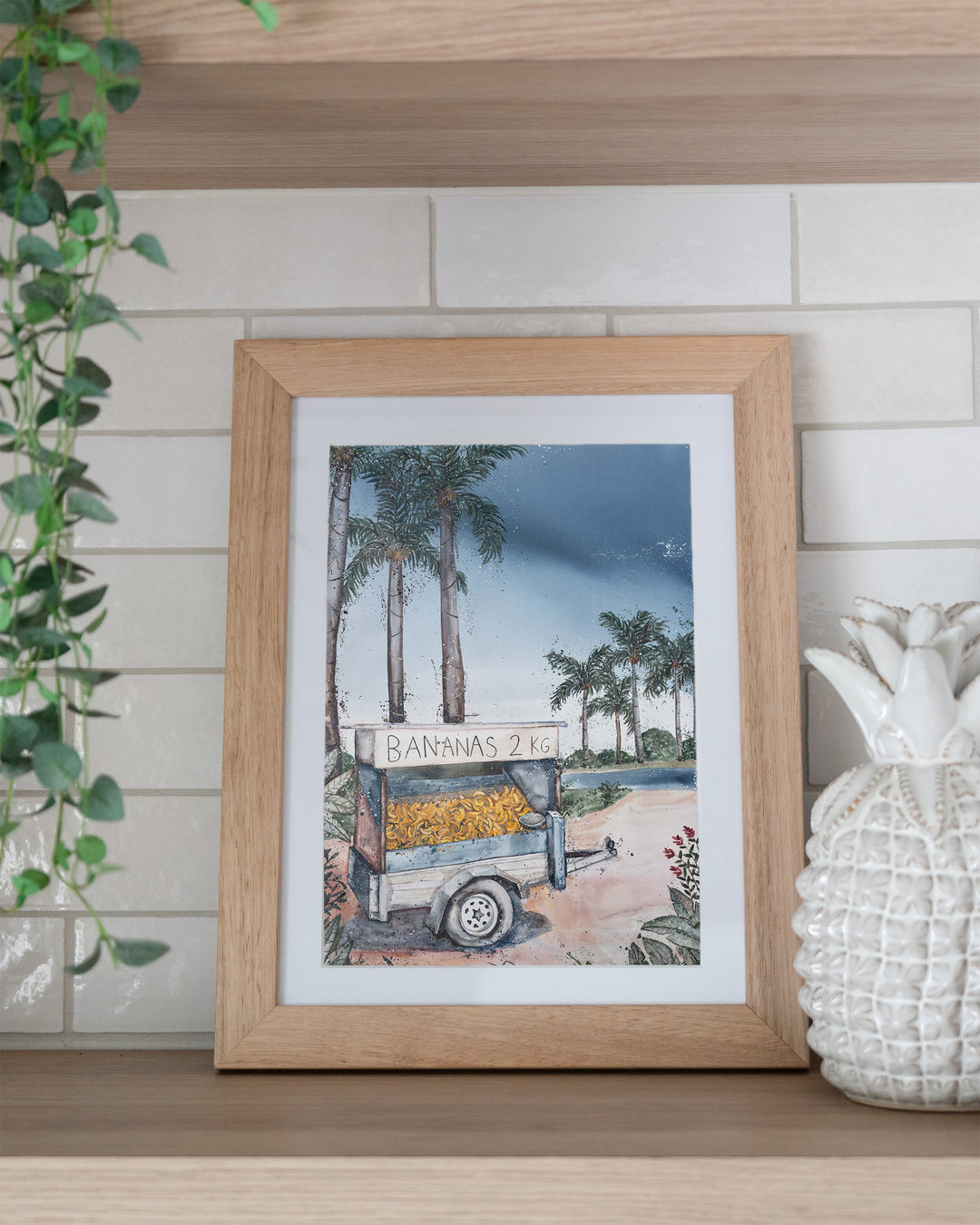 Banana Cart – tropical still life of a banana cart, framed paper print in oak frame, styled on a kitchen shelf