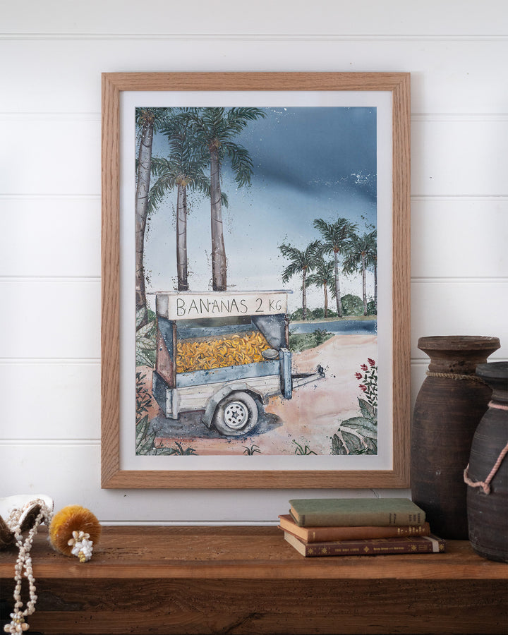 Banana Cart – tropical still life of a banana cart, framed paper print in oak frame, styled on a timber shelf