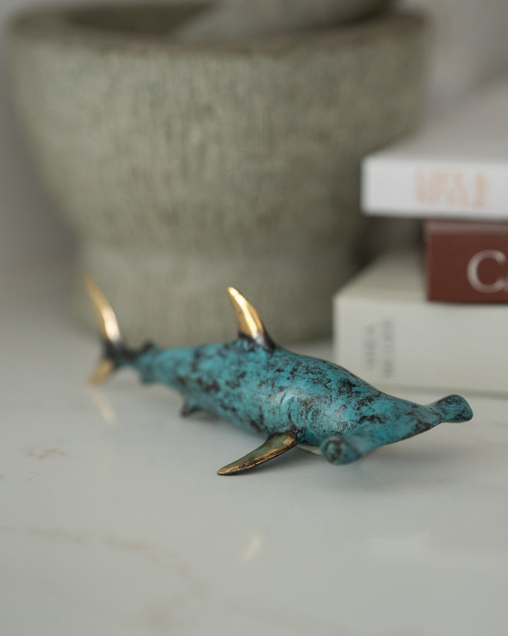 Hammerhead Shark sculpture in aged brass displayed next to books and a stone bowl on a shelf.