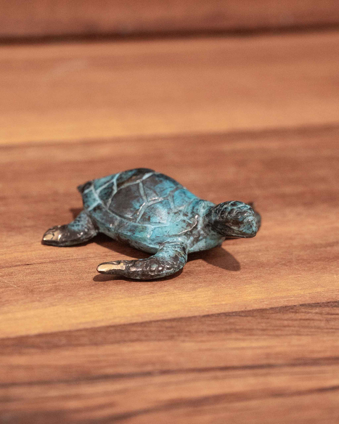 Hatchling Turtle sculpture made of aged brass with a weathered blue-green patina, resting on a wooden surface.