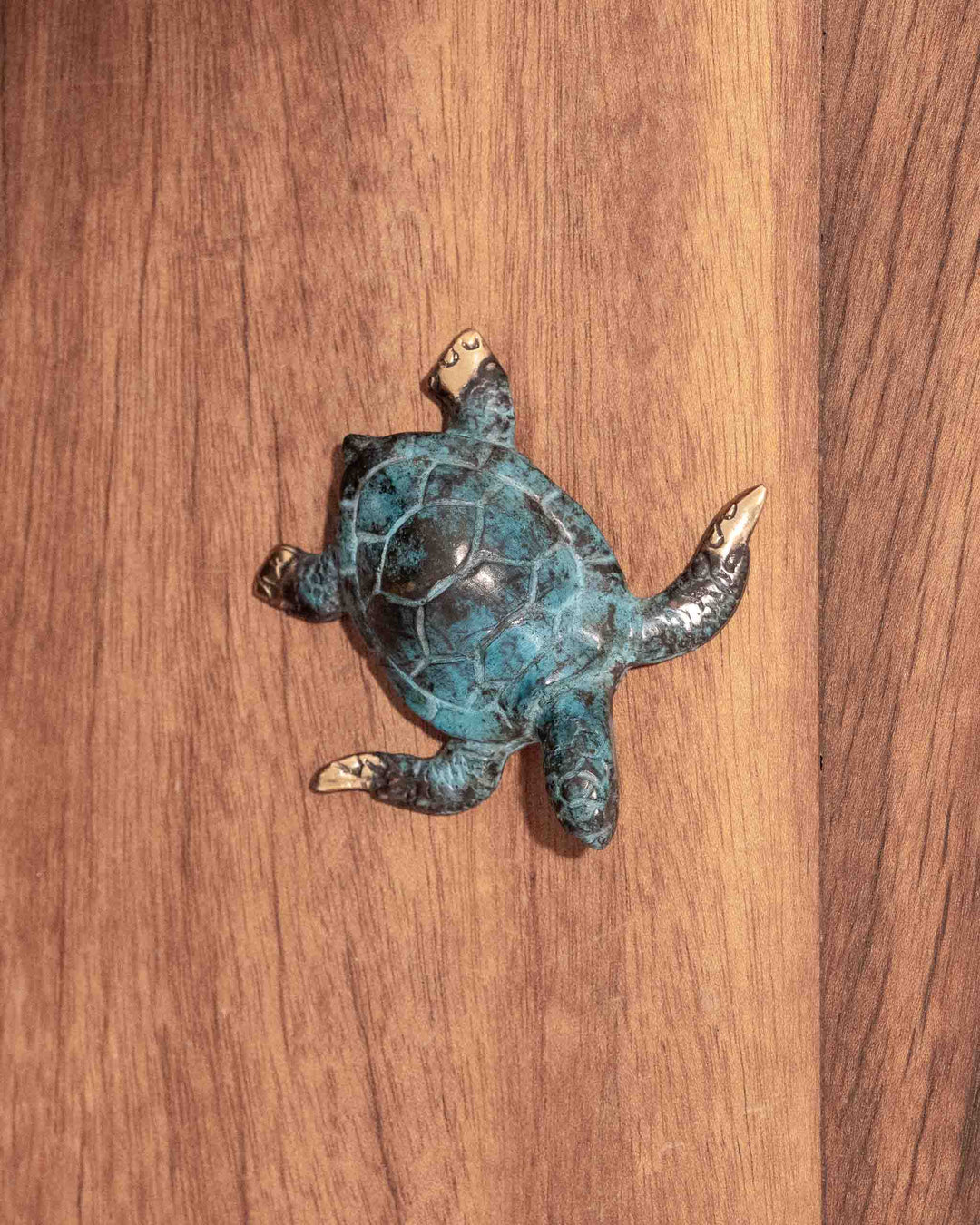 Hatchling Turtle sculpture in weathered blue and aged brass, resting on a wood surface.