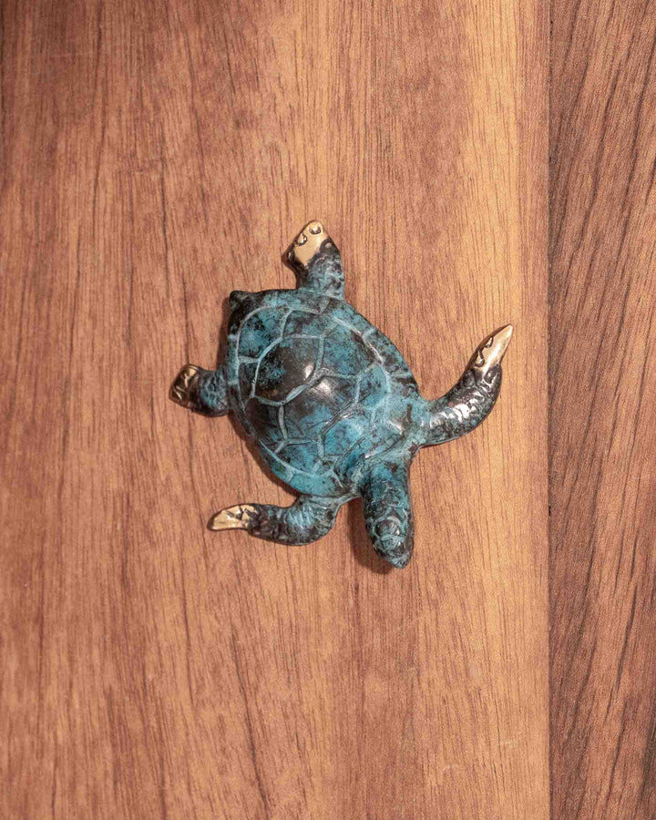 Hatchling Turtle sculpture in weathered blue and aged brass, resting on a wood surface.