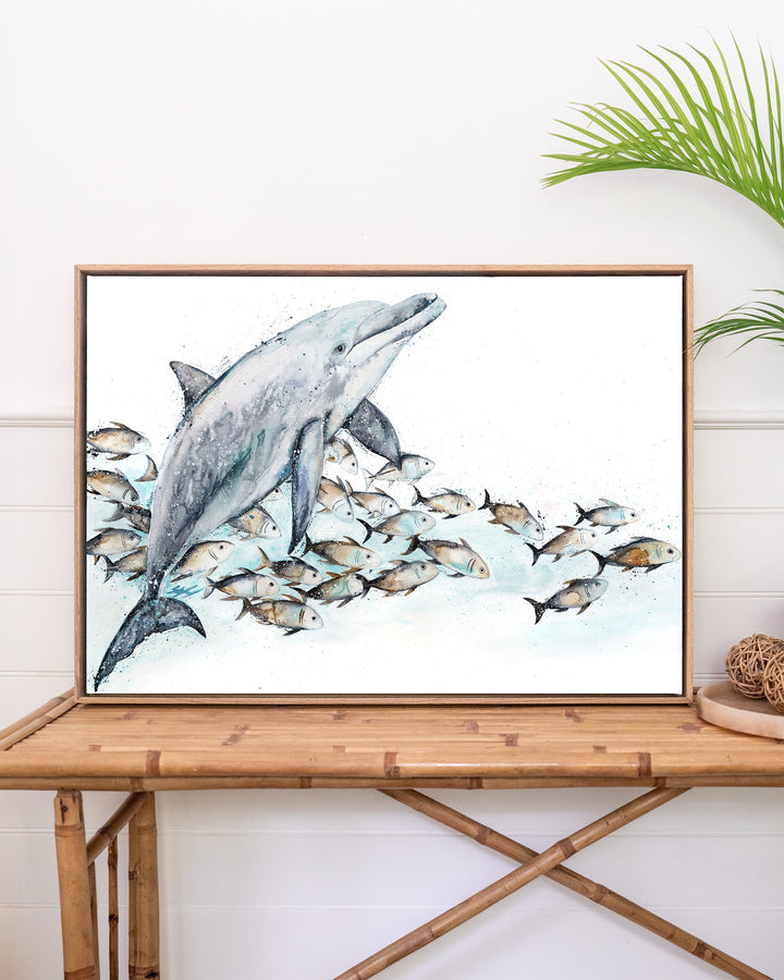 Bubble Toes – dolphin with a school of fish, framed canvas in oak float frame, styled on a rattan table