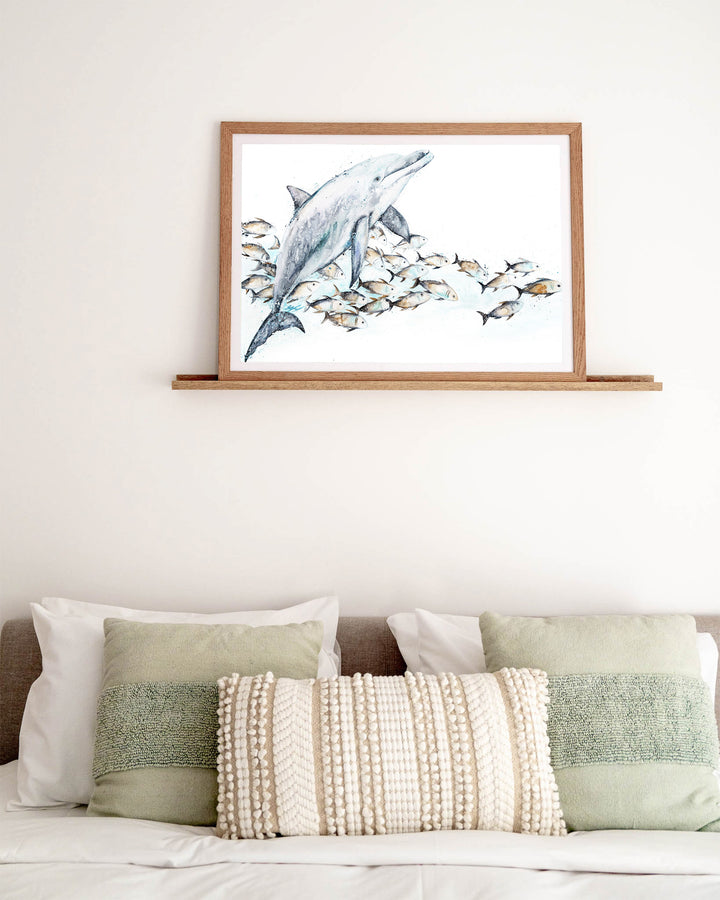 Bubble Toes – dolphin with a school of fish, framed paper print in oak frame, styled above a bed