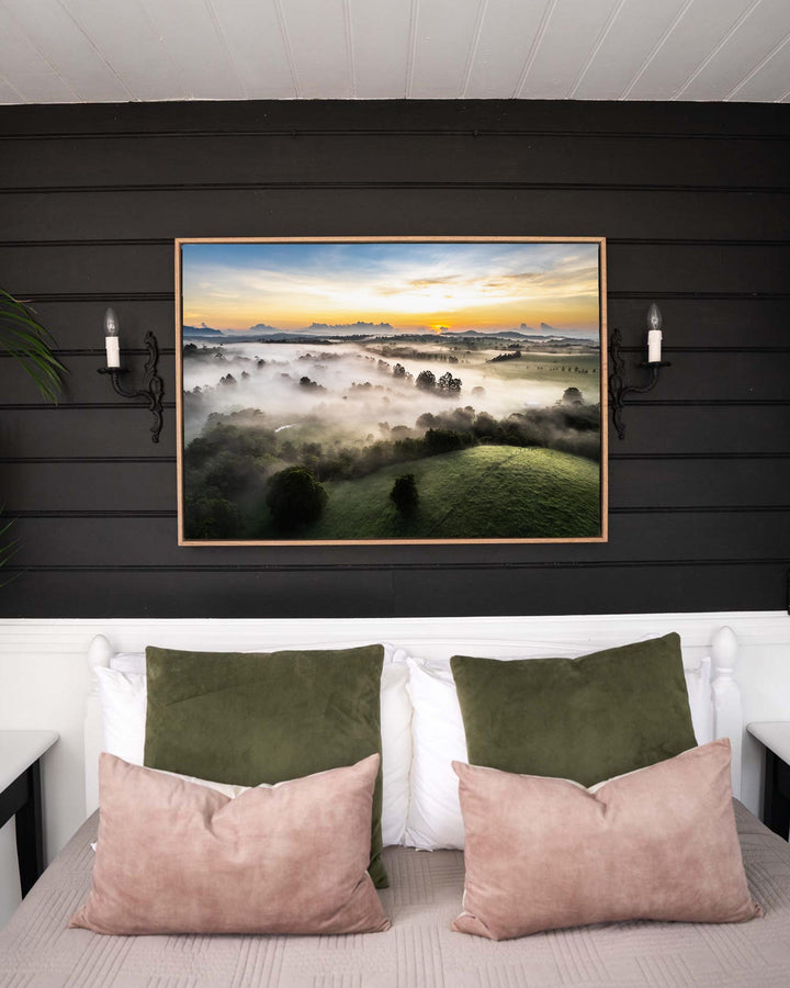 Aerial print of Atherton Tablelands, Campfire Smells and Fog Blankets, hanging above a bed with green and pink pillows.
