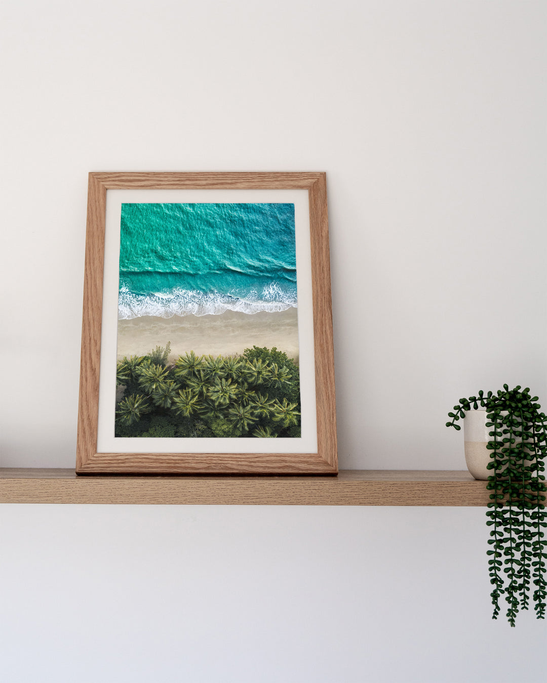 City of Palms – Four Mile Beach, Port Douglas, Aerial Photography by David Lloyd, framed paper print in oak frame, styled in a timber shelf setting