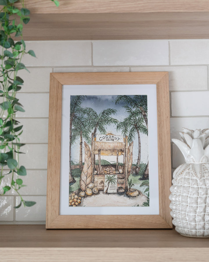Coconut Hut tropical still life fine art print by Stephanie Elizabeth, framed paper print in an oak frame on a kitchen shelf