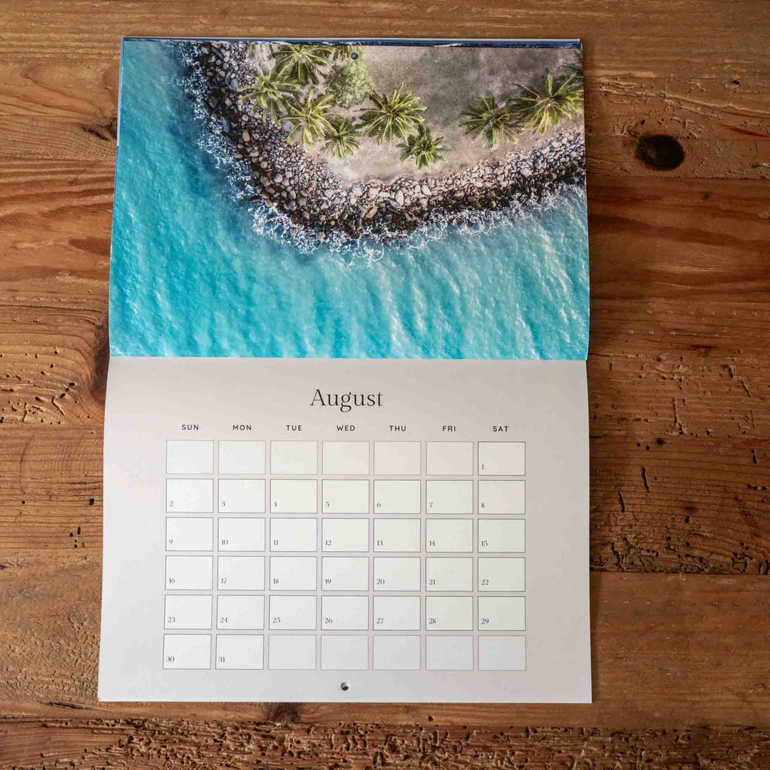 Calendar for August showing a tropical beach scene on a wooden surface