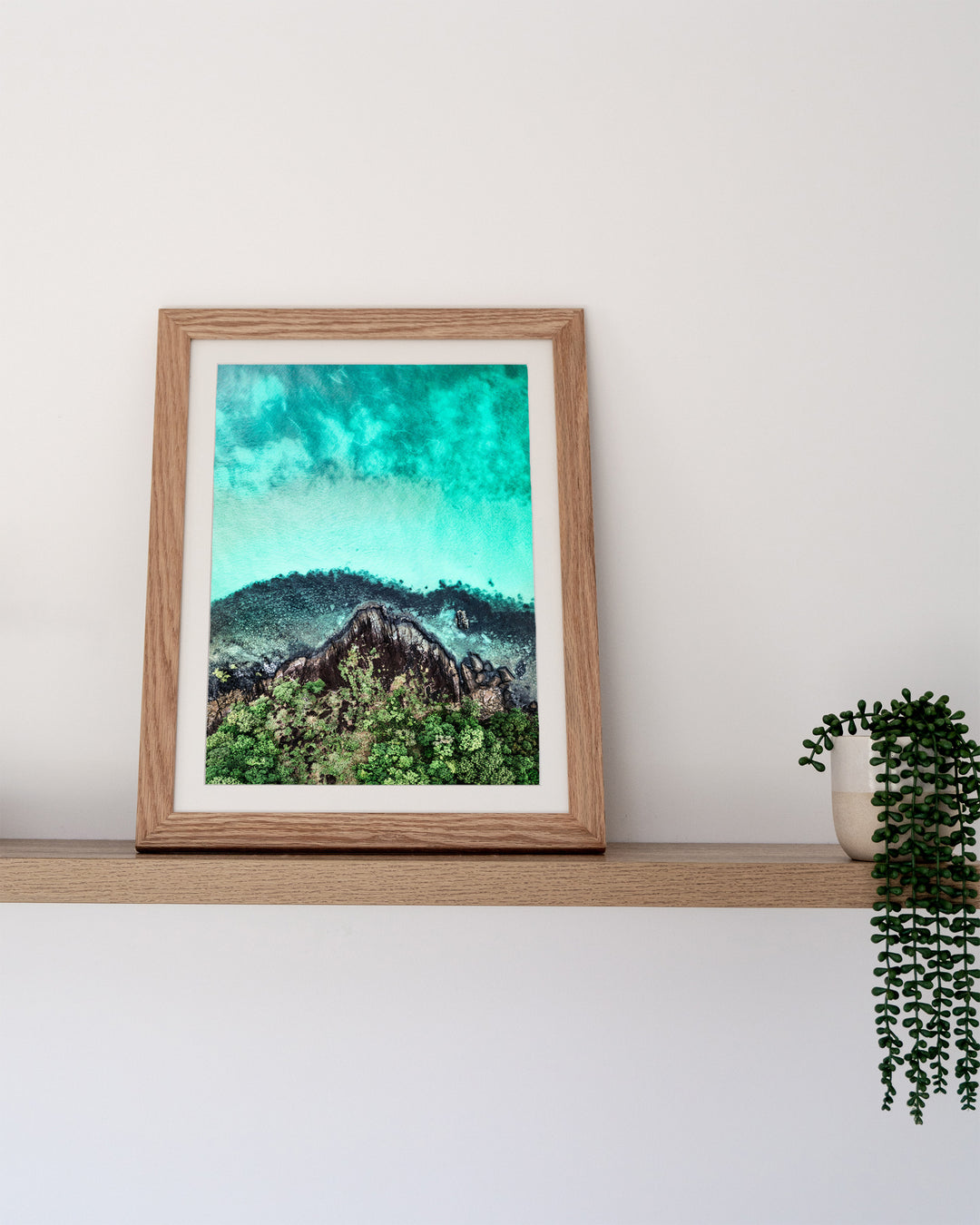 Fall At Your Feet – Cape Tribulation, Aerial Photography by David Lloyd, framed paper print in oak frame, styled in a timber shelf setting