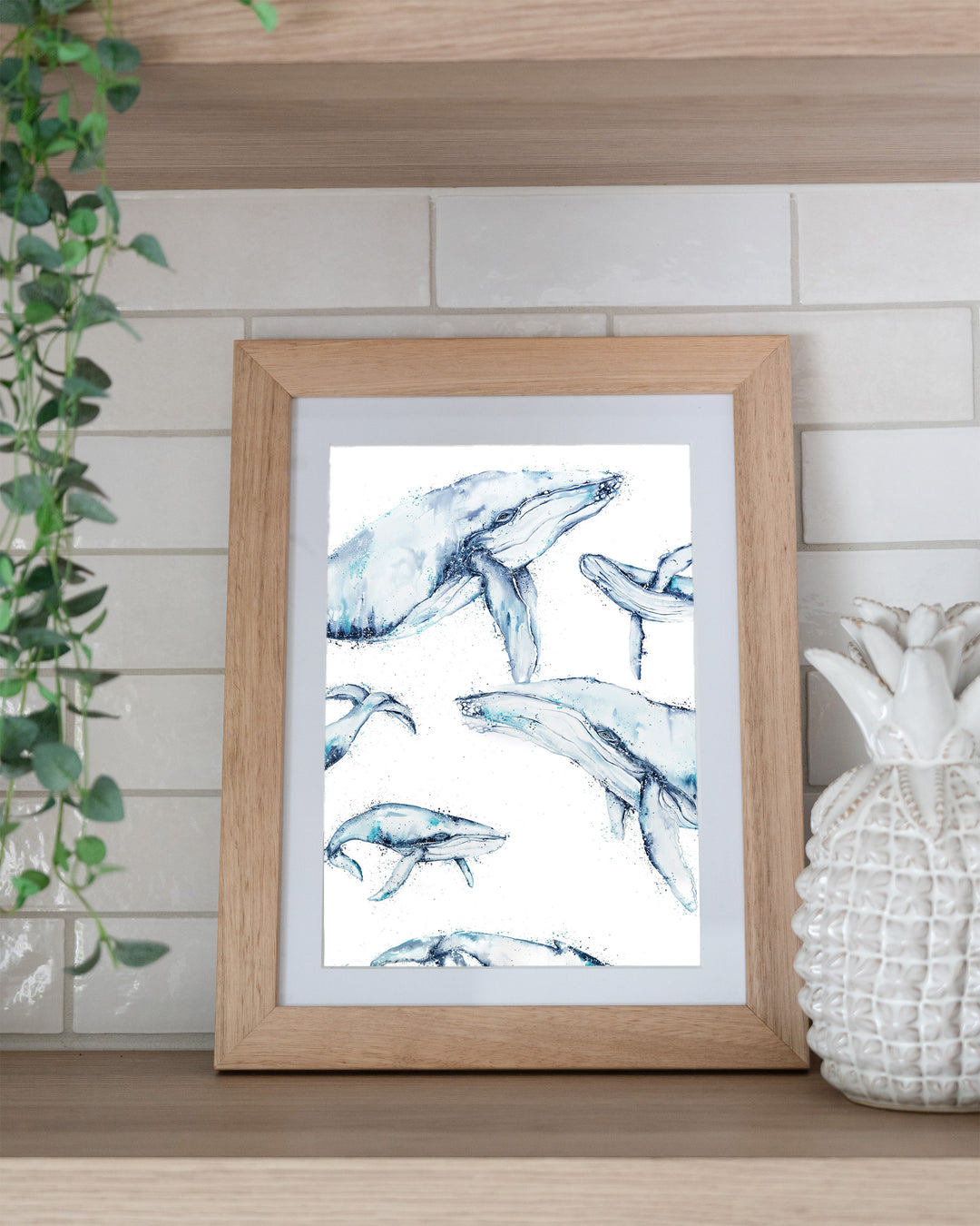 Family Trip – humpback whales, framed paper print in oak frame, styled on a kitchen shelf